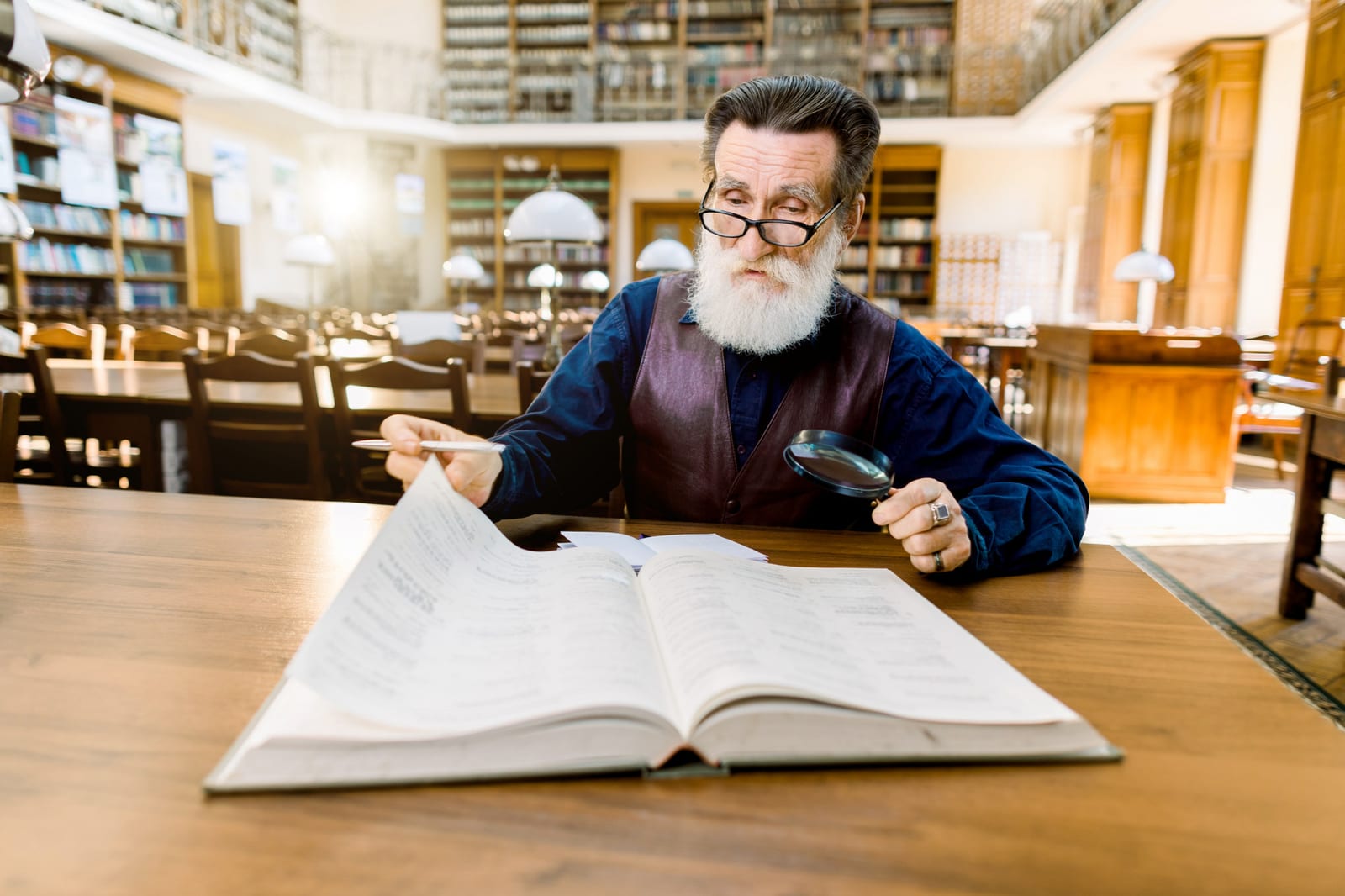 Bibliotecário examinando um grande volume encadernado com uma lupa, em uma sala de leitura cercada de estantes